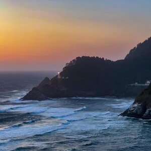 Puede incluir: Un paisaje costero al atardecer. La imagen presenta un faro en un acantilado rocoso, con olas rompiendo contra la orilla. El cielo transita del naranja al azul, y la escena está enmarcada por colinas boscosas.