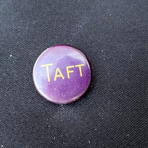 May include: Purple round button with the word "TAFT" in gold lettering.