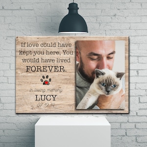 Op de afbeelding: Een houten gedenkdoek met een foto van een man die een kat vasthoudt. De tekst luidt "Als liefde je hier had kunnen houden, zou je VOOR ALTIJD hebben geleefd." met een pootprint en een rood hart. De tekst "in loving memory LUCY 07.19.14" is ook inbegrepen.