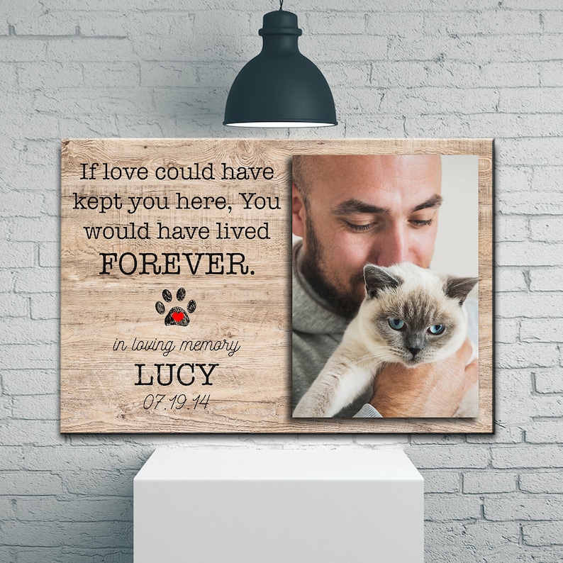 Op de afbeelding: Een houten gedenkdoek met een foto van een man die een kat vasthoudt. De tekst luidt "Als liefde je hier had kunnen houden, zou je VOOR ALTIJD hebben geleefd." met een pootprint en een rood hart. De tekst "in loving memory LUCY 07.19.14" is ook inbegrepen.