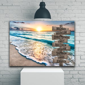 May include: A rectangular wall art print featuring a sunset beach scene with ocean waves washing onto the sand. A vertical wooden signpost stands on the right, displaying the names Michael, Madison, Christopher, Emily, Matthew, Briann, Shannon, Emma, and Jennifer.