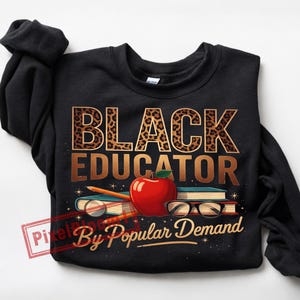 May include: Black sweatshirt with the words "BLACK EDUCATOR" in leopard print and gold lettering. Below the text is a red apple, books, pencils, and glasses. The text "By Popular Demand" is written in gold script.