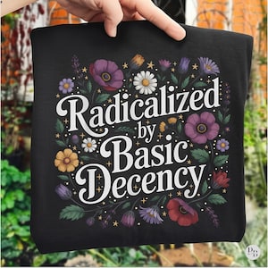 May include: Black tote bag featuring the text "Radicalized by Basic Decency" in white script. The design includes a floral arrangement with purple, yellow, red, and white flowers and green leaves.