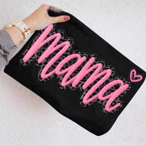 May include: Black fabric with the word "Mama" in bright pink, outlined with a gray leopard print design. A small pink heart is next to the word. The fabric is being held up by a person.