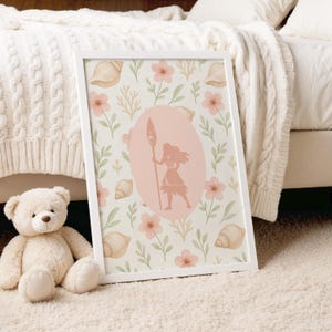 Op de afbeelding: Een ingelijste kunstdruk met een roze silhouet van een vrouw met een speer, in een roze ovaal. De achtergrond is crème met roze bloemen, schelpen en groene bladeren. Een teddybeer staat links.