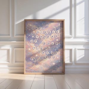 Puede incluir: Una impresión artística enmarcada con el texto "ONE SINGLE THREAD OF GOLD TIED ME TO YOU" en una fuente circular. El fondo presenta un cielo soñador y colorido con nubes arremolinadas y estrellas. El marco es de color marrón claro.