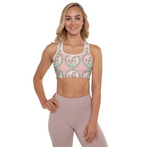 May include: A pink and green sports bra with a repeating pattern of pastel green horses in white and pink circles. The bra has a white band around the top and a racerback style.