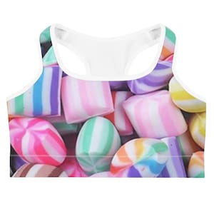 May include: A white-trimmed sports bra featuring a colorful candy pattern. The design includes various candies in shades of pink, green, purple, and yellow. The bra has a racerback style and is made of a soft, comfortable material.