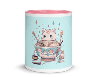 Può includere: Una tazza in ceramica bianca con un bordo rosa presenta un'illustrazione di cartone animato di un gatto bianco con orecchie rosa e un naso rosa, seduto in una ciotola blu di ramen. Il gatto è circondato da stelle e altri gatti più piccoli.