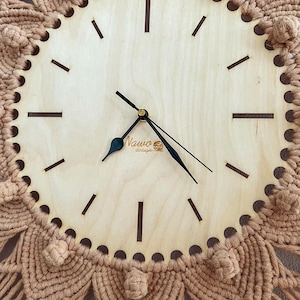 May include: A wooden clock with black hands and a brown macrame border. The clock face has a simple design with black hour markers and the text "Nauwo design" in the center.