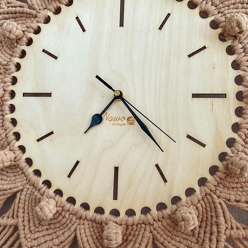 May include: A wooden clock with black hands and a brown macrame border. The clock face has a simple design with black hour markers and the text "Nauwo design" in the center.
