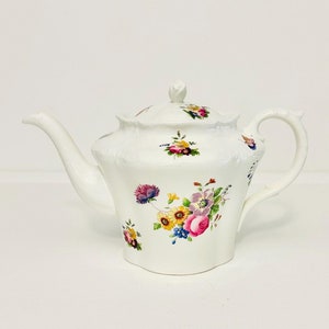 May include: A white porcelain teapot with a floral design. The teapot features a delicate floral pattern in shades of pink, yellow, blue, and green.