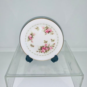 May include: A small white porcelain plate with a gold rim and a floral design featuring pink roses and green leaves.