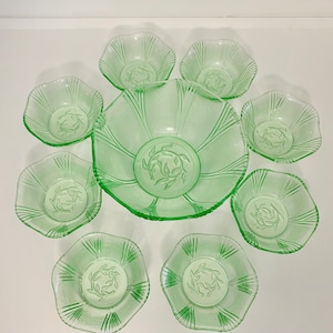 Op de afbeelding: Een set van acht groene glazen kommen, waaronder een grote serveerschaal en zeven kleinere kommen. De kommen hebben een gegolfde rand en een delicaat bloemenpatroon.