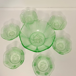 Op de afbeelding: Een set van zes groene glazen kommen met een delicaat bloemenmotief. De kommen zijn in verschillende maten, met een grote kom in het midden en vijf kleinere kommen eromheen.