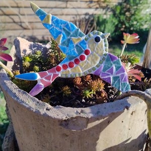 Peut inclure: Un colibri en mosaïque colorée, ornant un pot en béton vieilli. Les ailes et le corps du colibri sont composés de carreaux bleus, jaunes, rouges et violets. Le pot est rempli de verdure.
