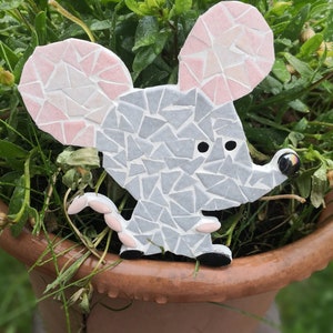 Peut inclure: Ornement de jardin en mosaïque représentant une souris. La souris est grise avec des oreilles roses et une queue rose. La souris a des yeux noirs et des pieds noirs. L'ornement est dans un pot marron avec des plantes vertes.