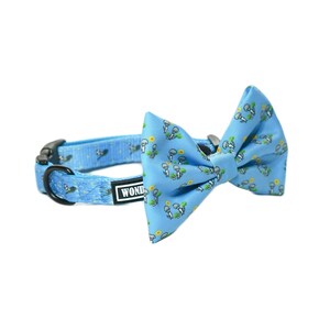 May include: A light blue dog collar and bow tie set. The collar and bow tie feature a repeating pattern of white cartoon dogs, yellow flowers, and green plants. The collar has a black buckle and a black metal ring.