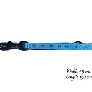 May include: A light blue dog leash with a black clasp and a black metal ring. The leash has a repeating pattern of soccer balls and is 1.5 cm wide and 150 cm long.