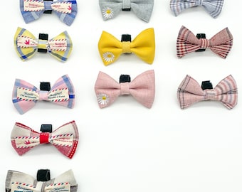 May include: Twelve different bow ties with various patterns and colors, including red, blue, yellow, pink, and white. Each bow tie has a small tag with French words like "Bonjour" and "Merci".