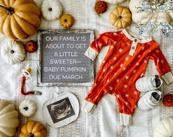May include: A letter board with the message "Our family is about to get a little sweeter - Baby Pumpkin Due March".  A small pumpkin-shaped plate with an ultrasound image is on the white blanket.  A baby onesie with a red and white snowflake pattern is on the blanket with a pair of white baby shoes.