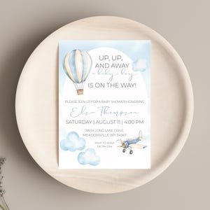 May include: A blue and white hot air balloon with a blue airplane and clouds on a light blue background. The text reads "Up, Up, And Away baby boy is on the way!"  Please join us for a baby shower honoring Else Thompson. Saturday, August 11, 4:00 PM. 78934 Long Lane Drive, Meadowville WY 34567. RSVP to Anna 555-555-1234.