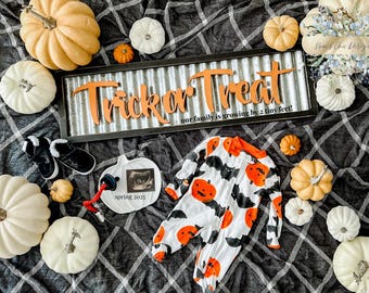 May include: A Halloween-themed announcement with pumpkins, baby shoes, and a onesie. The sign reads "Trick or Treat" and "our family is growing by 2 tiny feet!" A sonogram is displayed on a pumpkin-shaped plate.
