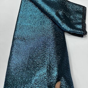 May include: Teal metallic fabric with a textured surface. The fabric has a slight sheen and is folded in half.