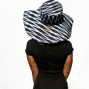 May include: A black and white zebra patterned sun hat with a wide brim. The hat has a gold logo that says "AMY'Z".