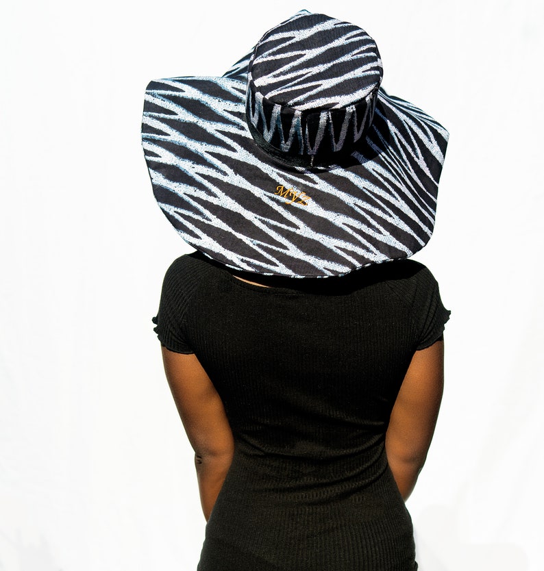 May include: A black and white zebra patterned sun hat with a wide brim. The hat has a gold logo that says "AMY'Z".