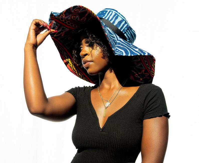 May include: A woman wearing a black shirt with a large, colorful sun hat with a blue and red patterned design. The hat has a wide brim and a black ribbon around the crown.