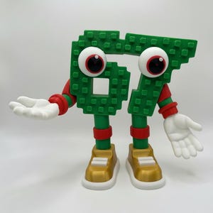May include: A whimsical green number 67 figure with large googly eyes, red accents, and white hands. The figure is wearing gold and white sneakers. The number is made of small square blocks.