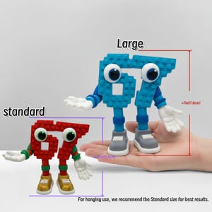 May include: Two toy figures shaped like the number 67, one red and one blue. The red figure is labeled "standard" and the blue figure is labeled "large". The large figure is approximately 7 inches (17.8cm) tall. The text says "For hanging use, we recommend the Standard size for best results."