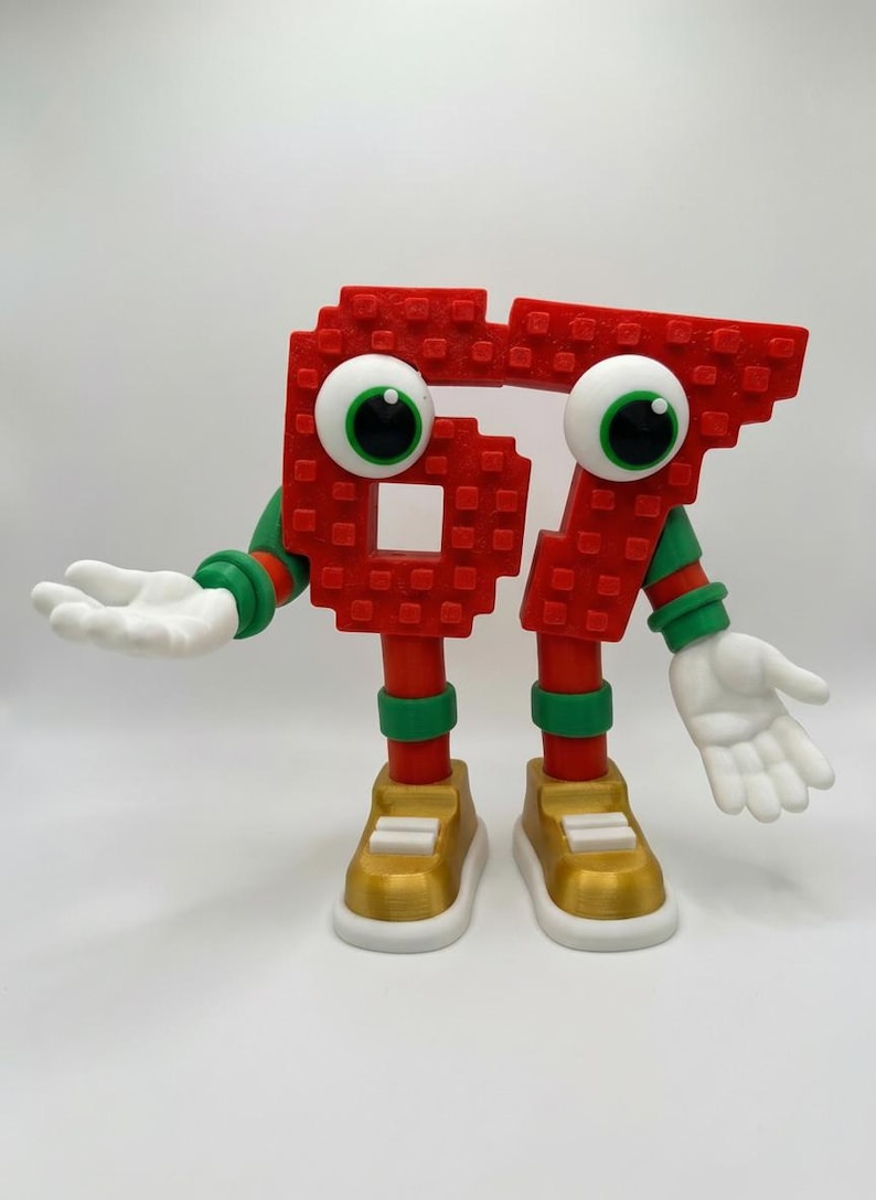 May include: A whimsical red number 67 figure with large googly eyes, white hands, and gold shoes. The figure has green and red accents on its arms and legs, and is posed with its hands open. The figure is a fun, playful design.