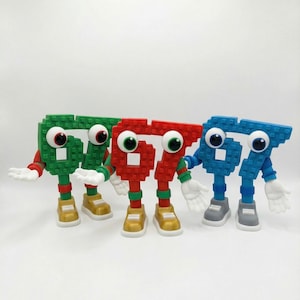 May include: Four colorful, anthropomorphic number seven figures. The figures are green, red, and blue, with white hands, large googly eyes, and gold or gray shoes. The figures are made of pixelated blocks.