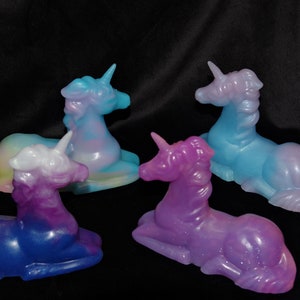 May include: Four iridescent unicorn figurines in various pastel colors, including blue, purple, pink, and yellow. The unicorns are lying down with their heads turned to the side.