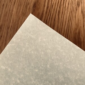 May include: A close-up of a light gray textured paper surface. The paper is placed on top of a brown wood surface.