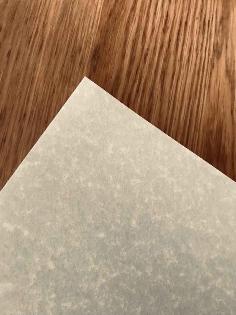 May include: A close-up of a light gray textured paper surface. The paper is placed on top of a brown wood surface.