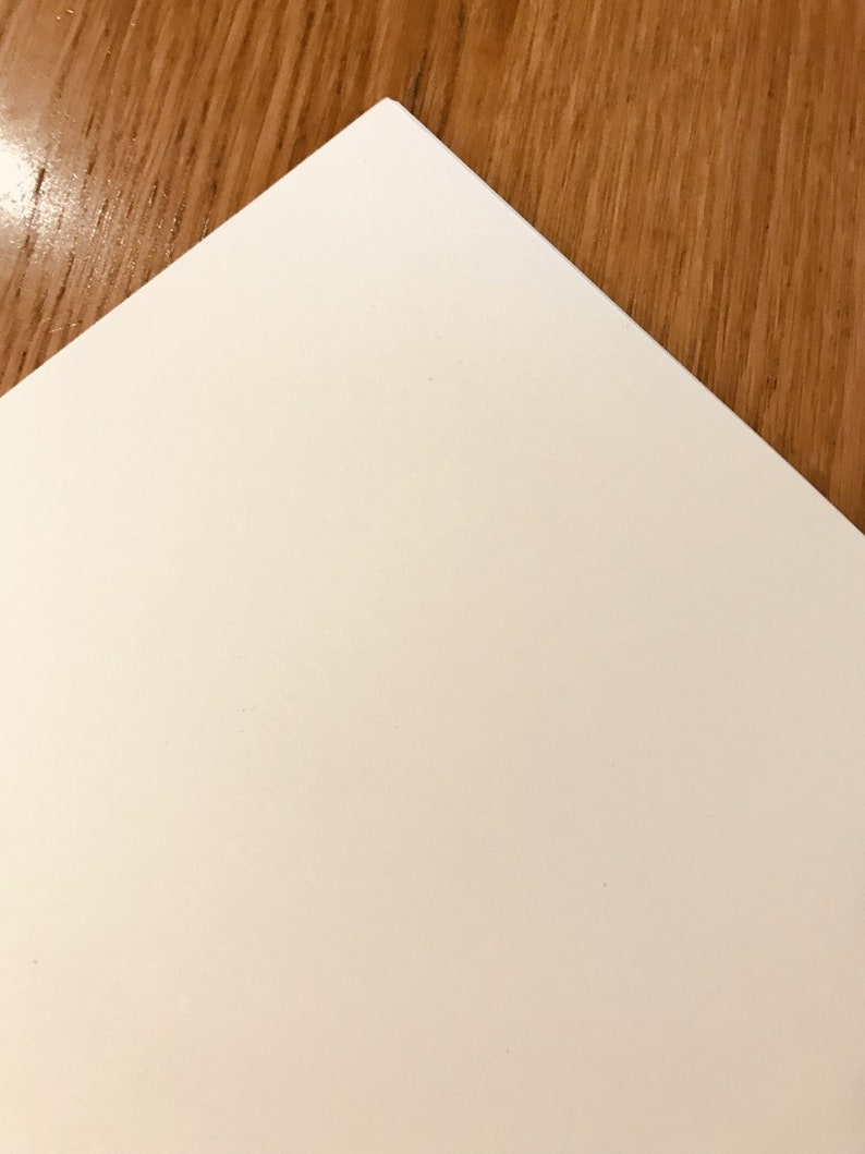 May include: A plain white sheet of paper, with a slightly textured surface, is lying on a wooden surface.