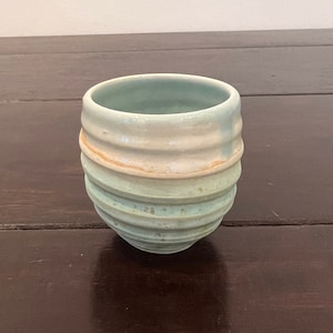 Può includere: Una tazza in ceramica fatta a mano con un design a coste. La tazza presenta una combinazione di colori azzurro e crema con un tocco di arancione. Un pezzo di ceramica unico.