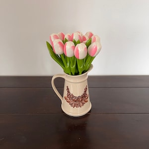 May include: A white ceramic jug with a brown floral design, filled with a bouquet of pink and white artificial tulips.