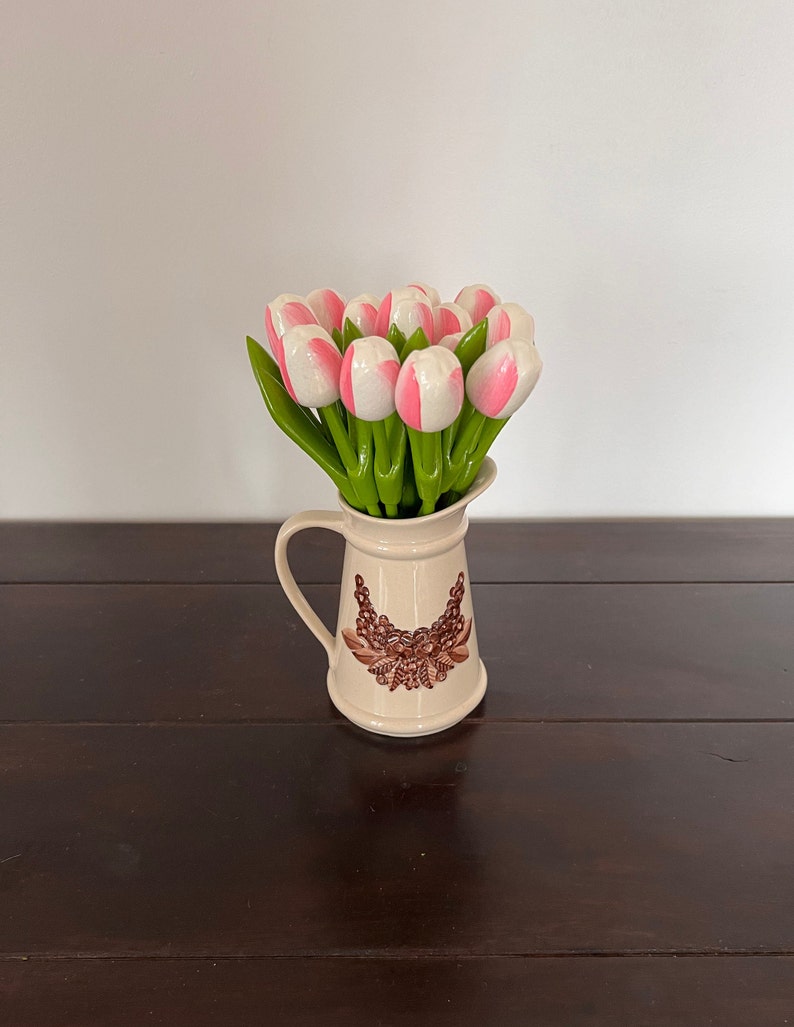 May include: A white ceramic jug with a brown floral design, filled with a bouquet of pink and white artificial tulips.