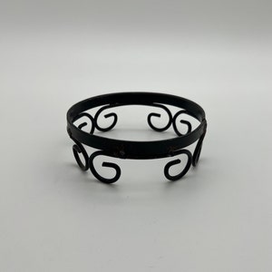 May include: Black metal ring stand with a decorative scroll design. The stand is circular and has four scrolls on the bottom.