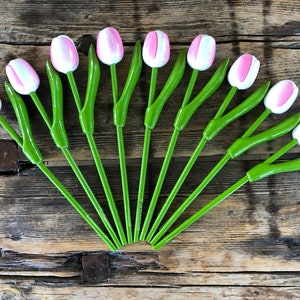 May include: A set of 12 wooden tulips with pink and white painted petals and green stems. The tulips are arranged in a fan shape on a wooden surface.