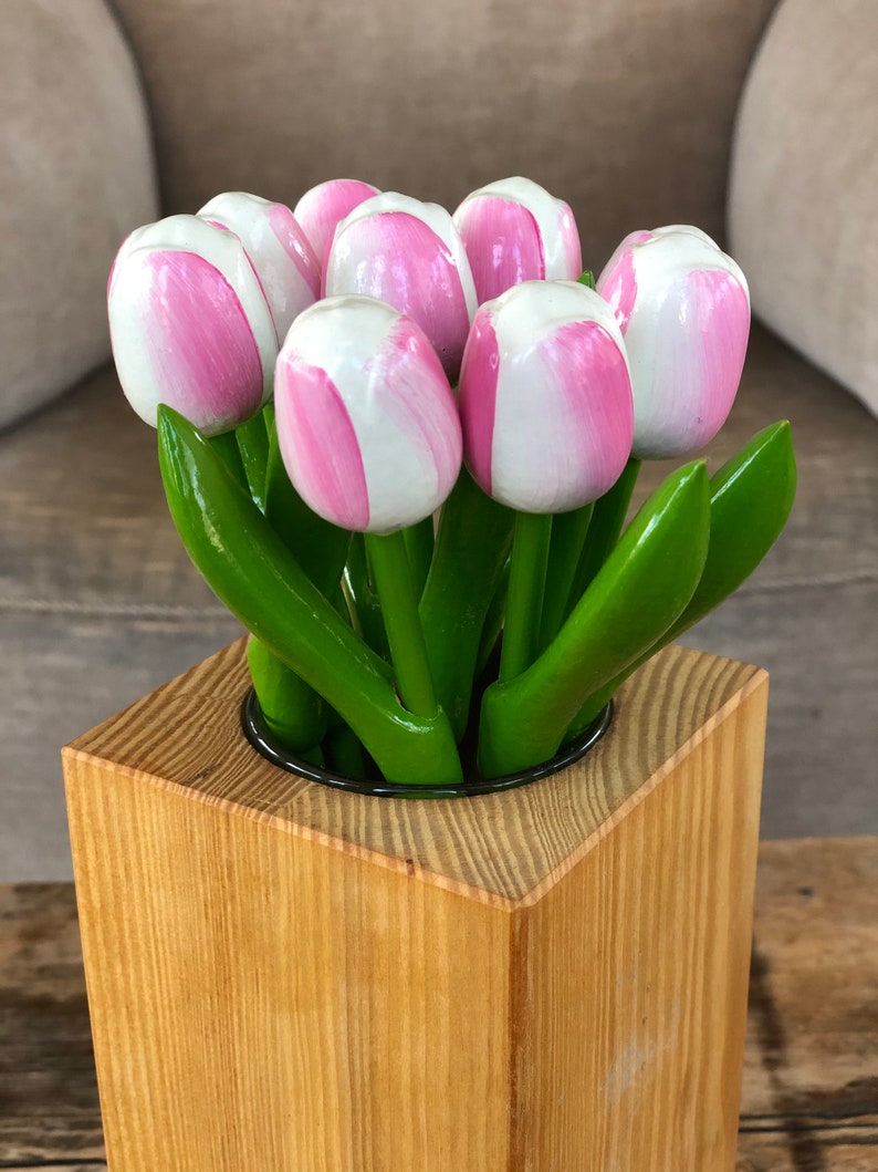 May include: A square wooden vase with a light brown finish. The vase is filled with a bouquet of pink and white wooden tulips.