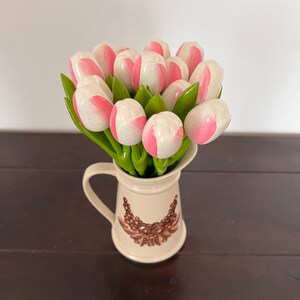 May include: A bouquet of pink and white wooden tulips in a cream-coloured pitcher with a brown floral design.