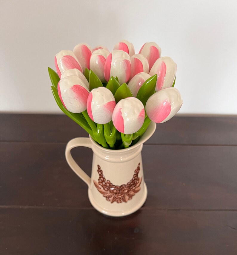 May include: A bouquet of pink and white wooden tulips in a cream-coloured pitcher with a brown floral design.