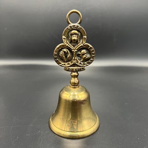Peut inclure: Une cloche en laiton avec un dessus en forme de trèfle représentant trois visages de singes et les mots "HEAR NO EVIL, SEE NO EVIL, SPEAK NO EVIL". La cloche a une boucle pour l'accrocher et un battant à l'intérieur.