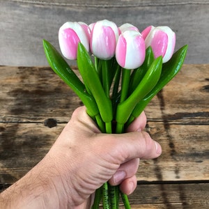 May include: A bouquet of wooden tulips with pink and white painted petals and green stems. The tulips are held in a hand.