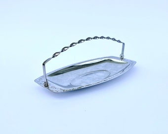 May include: A silver-colored serving tray with a decorative handle. The tray has a rectangular shape with rounded ends and a patterned border. The handle is twisted and adds a unique design element. The tray is likely made of metal.